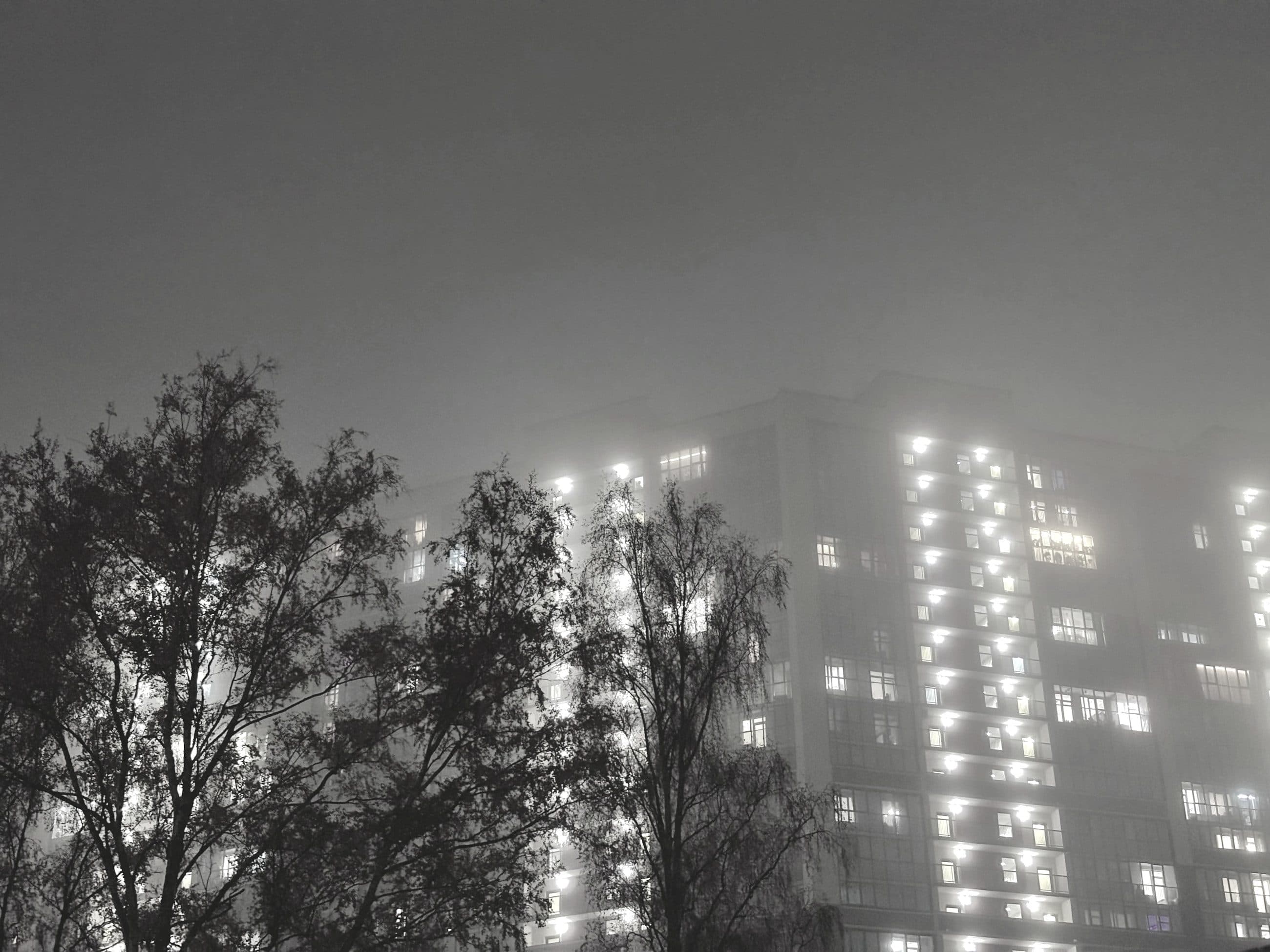 Torre residencial com janelas acesas, envolta em neblina à noite